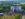 An aerial view shows attendees gathered at Philadelphia’s FIFA Fan Festival around a large stage and video screen. Set within a green park landscape near the Delaware River, the event features live entertainment, fan activities, and FIFA World Cup 26 branding throughout the festival grounds.