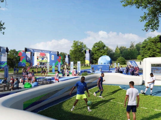 Des visiteurs jouent un match de football sur un petit terrain lors du Fan Festival de la Coupe du Monde de la FIFA 2026 à Philadelphie, avec la foule, les activités interactives et une grande scène visible à l'arrière-plan.