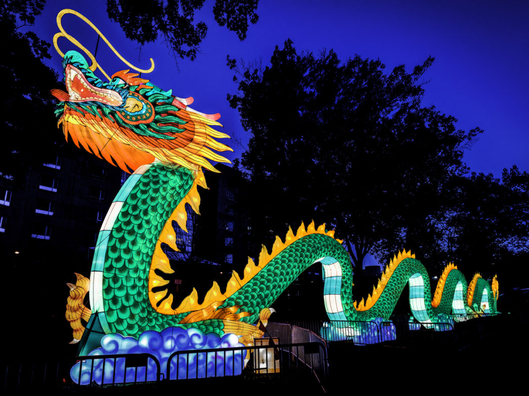 A giant illuminated green dragon lantern winds through the night at Philadelphia’s Chinese Lantern Festival, glowing against a deep blue evening sky.