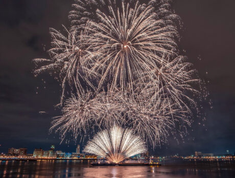 Bright white fireworks burst above the Delaware River Waterfront during an Independence Day celebration, illuminating the night sky and reflecting on the water with the Philadelphia skyline in the background.