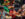 Four men in colorful traditional African-inspired clothing play hand drums on an outdoor stage area during the Juneteenth Festival in Philadelphia. Bright red, green, yellow, and black decorations and floral arrangements fill the background, creating a festive atmosphere as performers celebrate Black culture and heritage through music and community gathering.