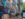 **Alt text:** A group of pedestrians walks along a Center City sidewalk beside a vibrant mural celebrating Philadelphia landmarks, culture and history. The colorful artwork stretches down the block near a bus shelter and modern office buildings.