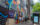 **Alt text:** A group of pedestrians walks along a Center City sidewalk beside a vibrant mural celebrating Philadelphia landmarks, culture and history. The colorful artwork stretches down the block near a bus shelter and modern office buildings.