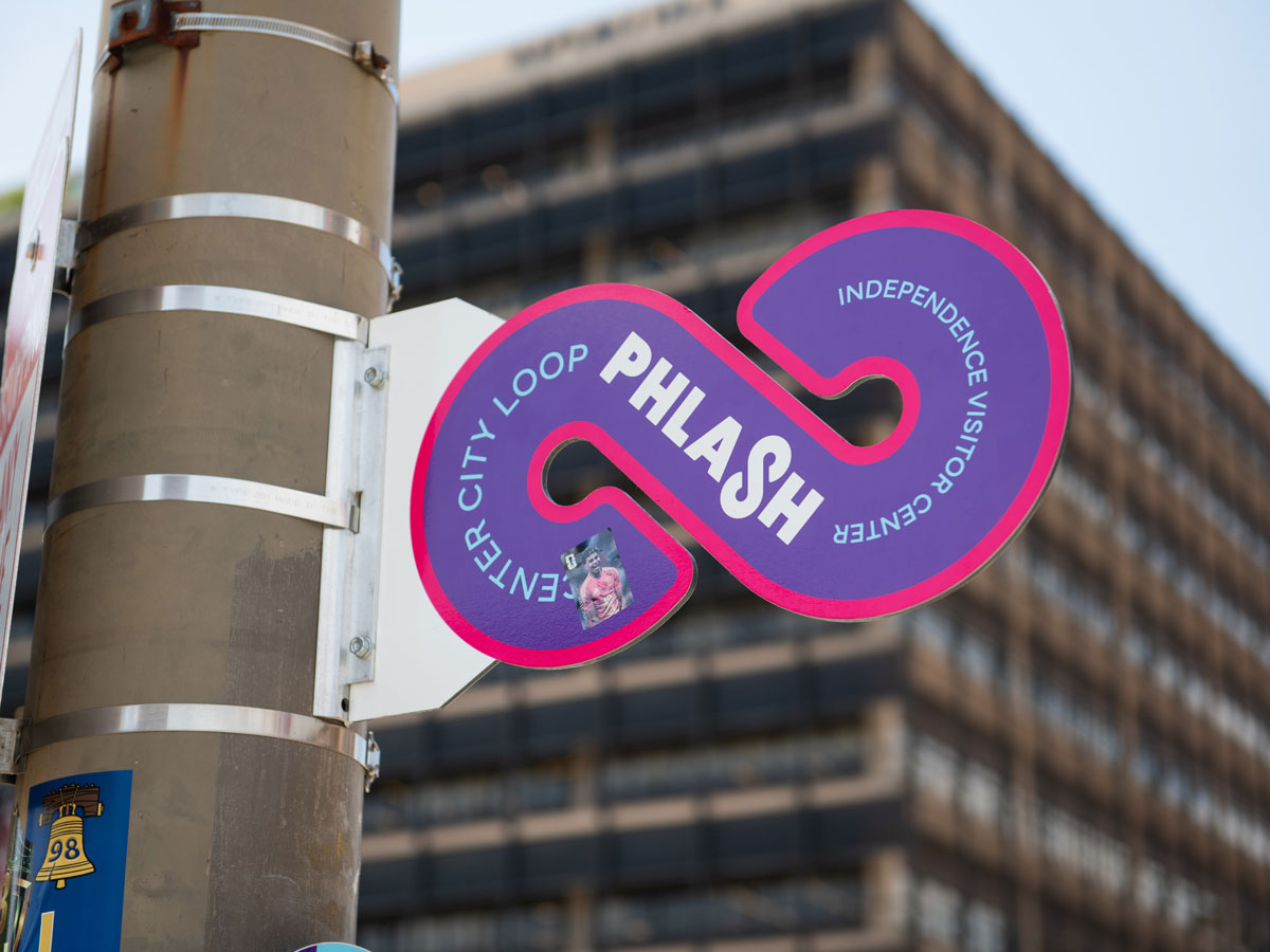 Un colorido letrero circular de PHLASH instalado en un poste de la calle en el centro de Filadelfia, con una calcomanía del futbolista español Lamine Yamal pegada en él.