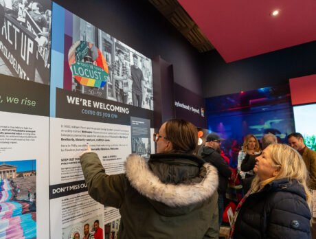 Les visiteurs découvrent les expositions du centre d'accueil Philly Pride, en lisant les panneaux consacrés à l'histoire et à la culture de Philadelphie, tandis que des écrans interactifs et des graphismes colorés sur le thème de la Pride agrémentent cet espace accueillant.