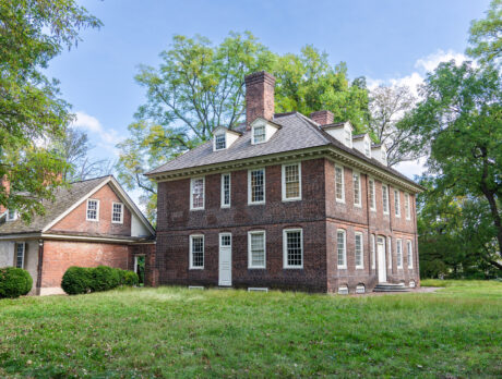 Stenton, a historic 18th-century brick mansion in Philadelphia’s Germantown neighborhood, stands amid a grassy lawn and mature trees. The Georgian-style house features a steep roof, dormer windows, and tall chimneys, highlighting its well-preserved colonial architecture.