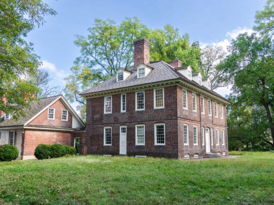 Stenton, un manoir historique en briques du XVIIIe siècle situé dans le quartier de Germantown à Philadelphie, se dresse au milieu d'une pelouse et d'arbres matures. La maison de style géorgien présente un toit pentu, des lucarnes et de hautes cheminées, mettant en valeur son architecture coloniale bien préservée.