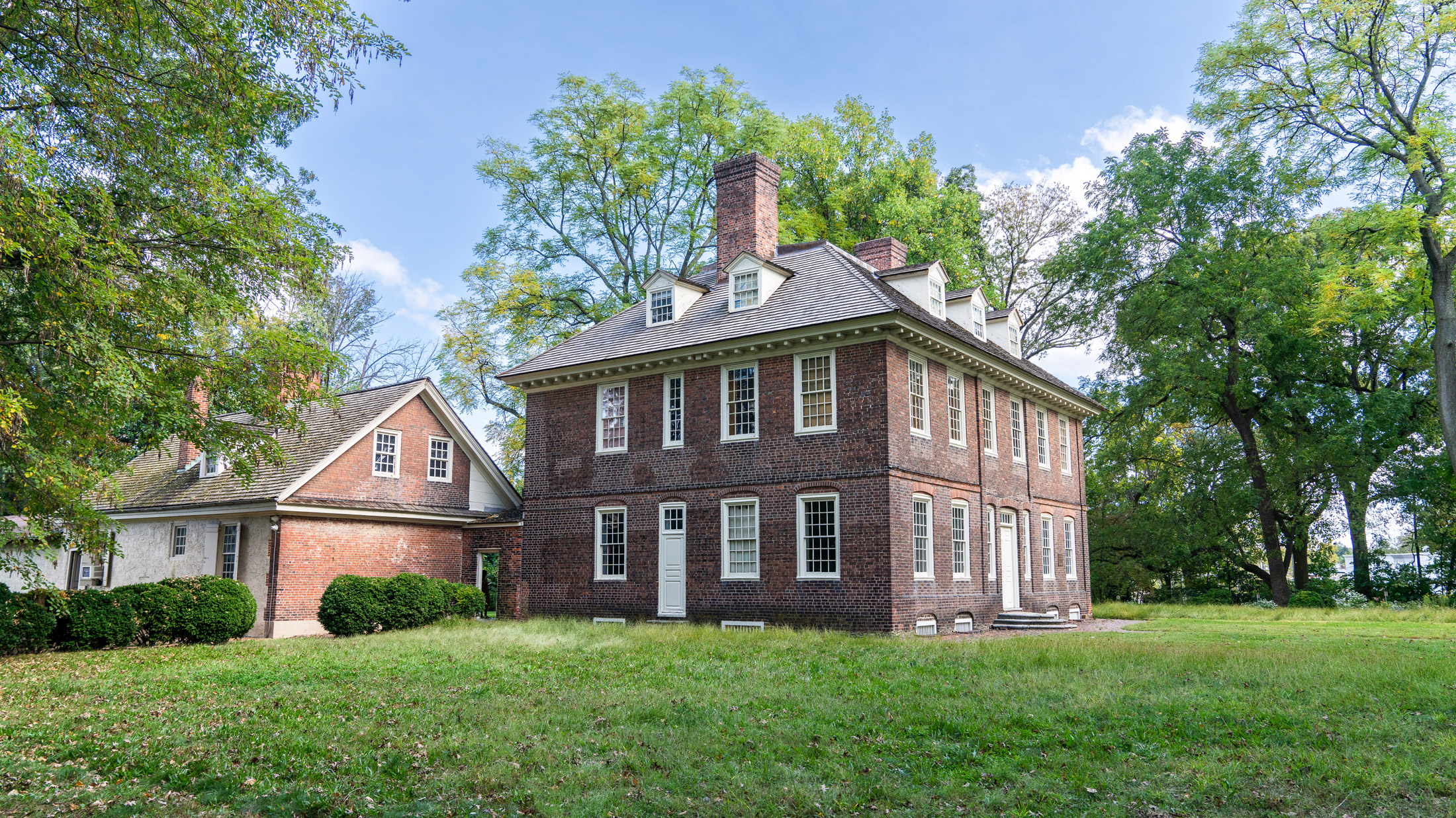 Stenton, un manoir historique en briques du XVIIIe siècle situé dans le quartier de Germantown à Philadelphie, se dresse au milieu d'une pelouse et d'arbres matures. La maison de style géorgien présente un toit pentu, des lucarnes et de hautes cheminées, mettant en valeur son architecture coloniale bien préservée.