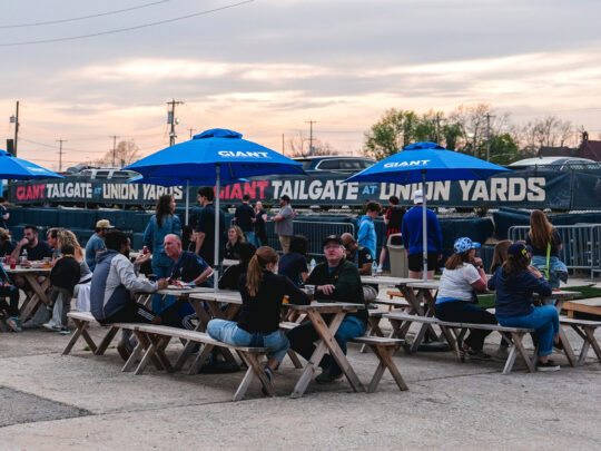 Los visitantes se reúnen en las mesas de picnic bajo las sombrillas azules en Union Yards, un espacio al aire libre para fiestas previas a los partidos y eventos situado junto al estadio del Philadelphia Union, el Subaru Park, en Chester, Pensilvania.
