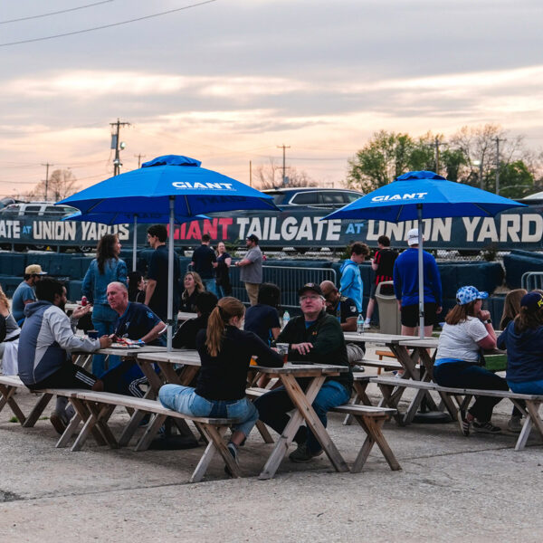Los visitantes se reúnen en las mesas de picnic bajo las sombrillas azules en Union Yards, un espacio al aire libre para fiestas previas a los partidos y eventos situado junto al estadio del Philadelphia Union, el Subaru Park, en Chester, Pensilvania.