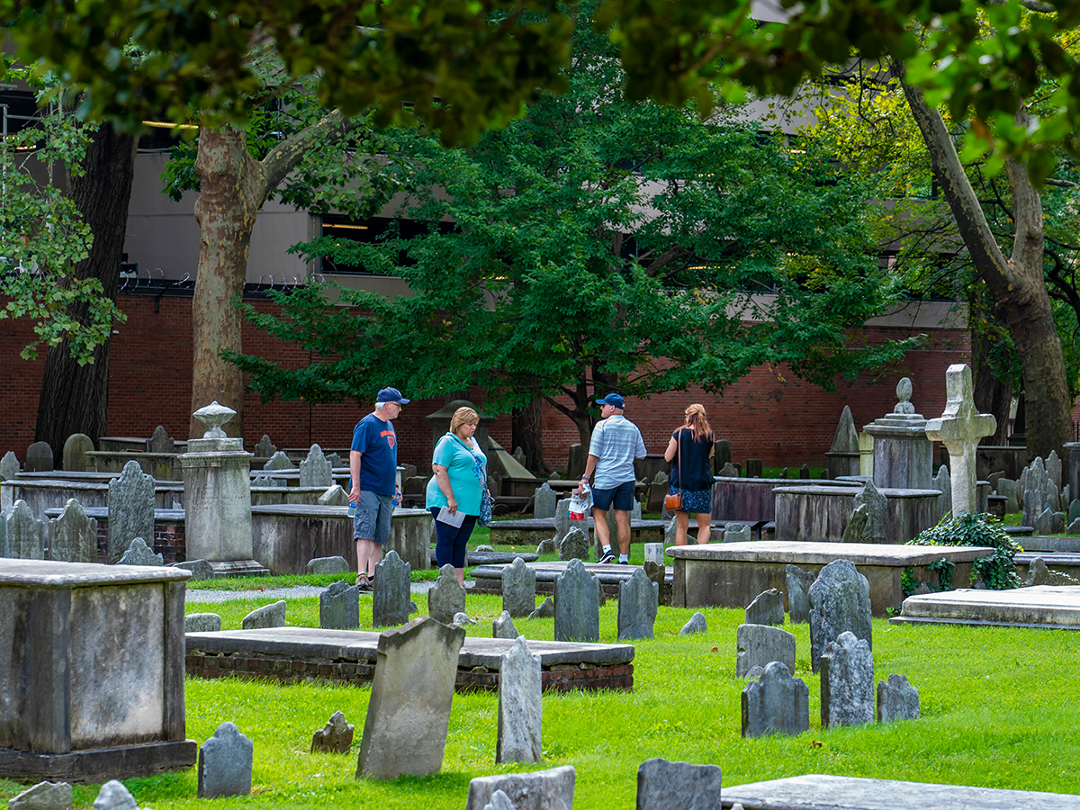 Visitors walk through the Christ Church Burial Ground, featuring historic headstones and burial plots in a grass lawn.