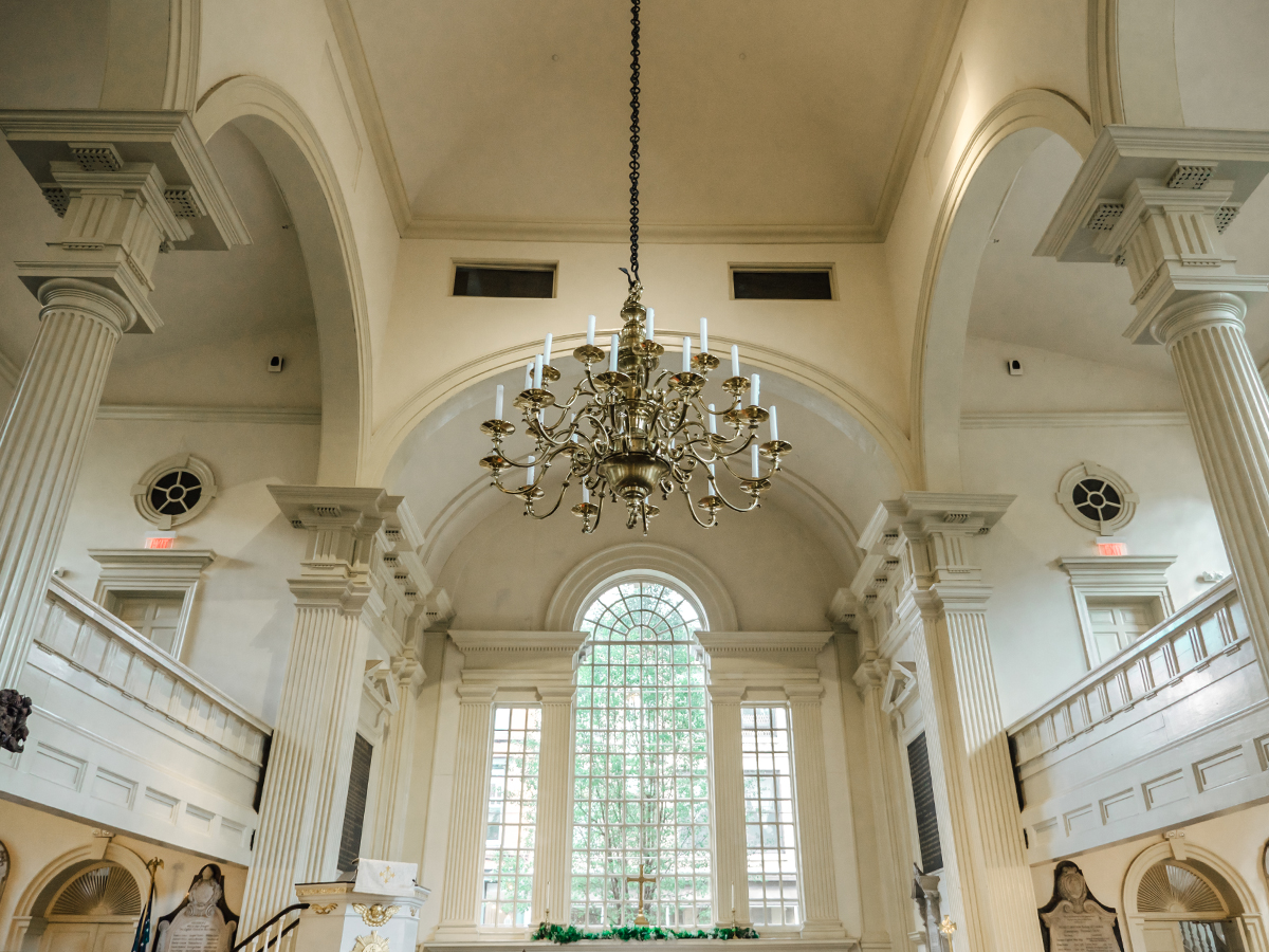 A brass chandelier with white candlesticks hangs beneath soaring arches and tall windows inside the historic Christ Church in Philadelphia.