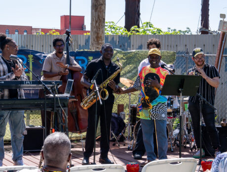 Members of a jazz ensemble clap while the saxophonist receives recognition while on on outdoor stage at the Coltrane 100 launch event.