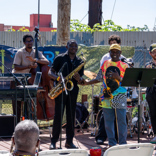 Leden van een jazzensemble klappen terwijl de saxofonist in het zonnetje wordt gezet op het openluchtpodium tijdens het evenement ter gelegenheid van de lancering van Coltrane 100.