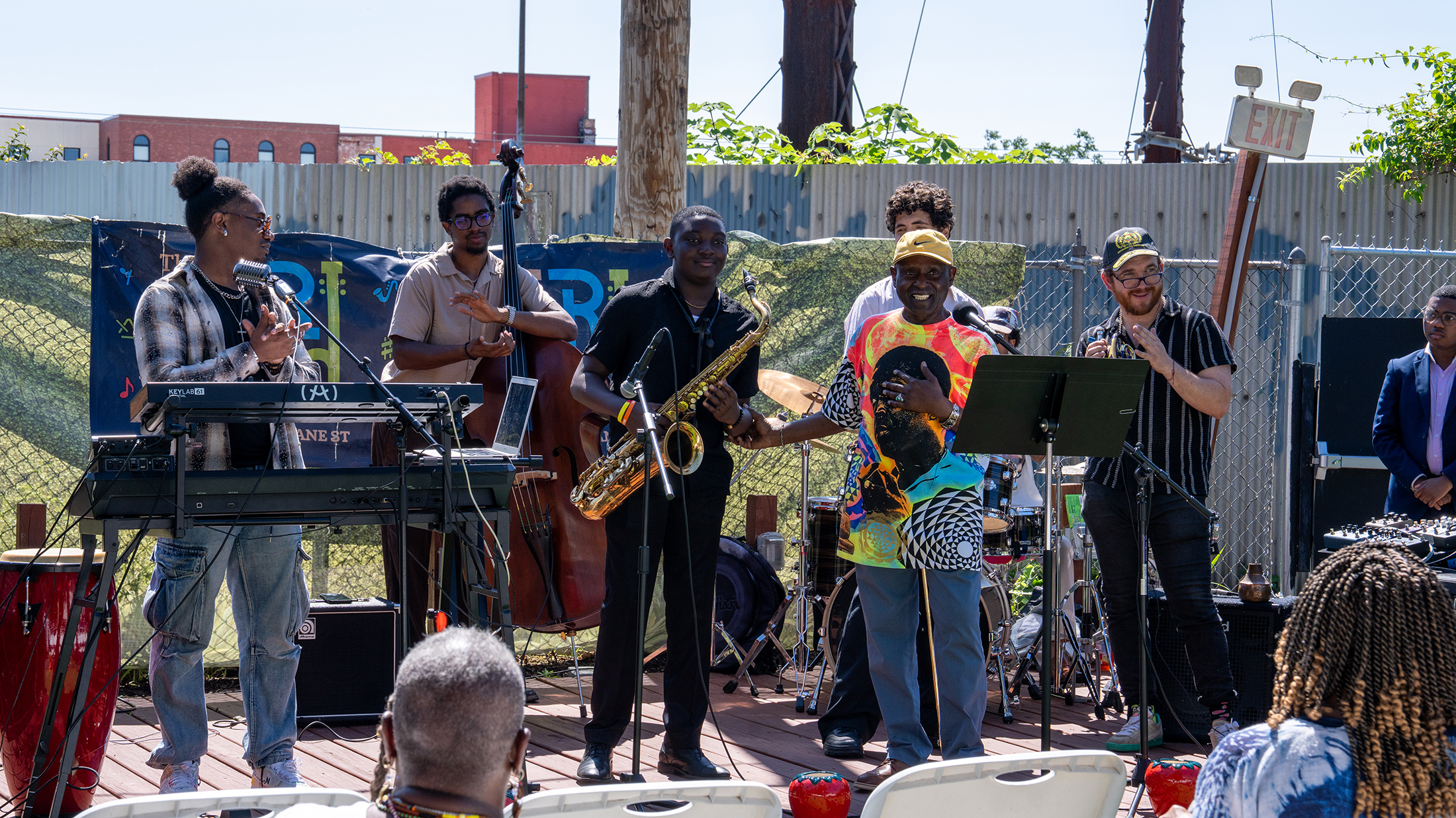 Los integrantes de un grupo de jazz aplauden mientras el saxofonista recibe un reconocimiento en el escenario al aire libre durante el evento de lanzamiento de «Coltrane 100».