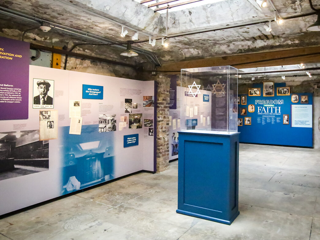 An exhibition gallery inside Eastern State Penitentiary features interpretive panels, historic photographs and artifacts, including the Star of David in a glass display.