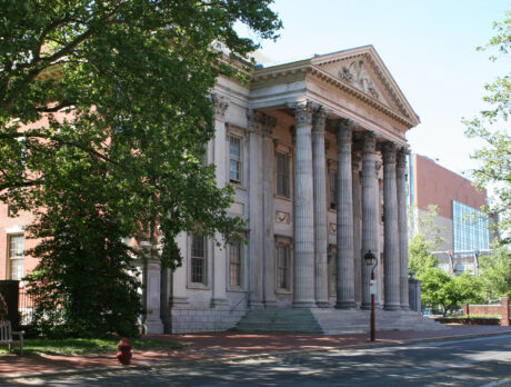 The grand front of the First Bank of the United States shows its stately row of columns and symmetrical stone architecture under a bright blue sky.