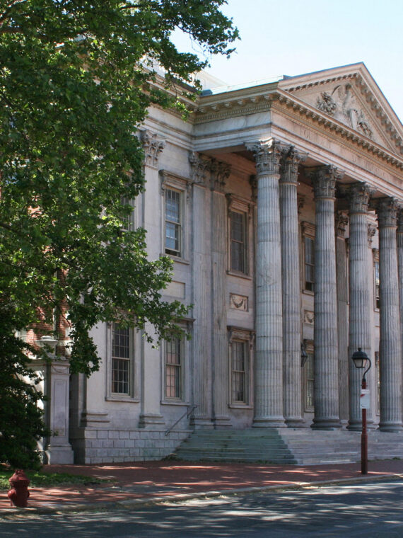 La majestuosa fachada del Primer Banco de los Estados Unidos luce su imponente hilera de columnas y su arquitectura simétrica de piedra bajo un cielo azul brillante.