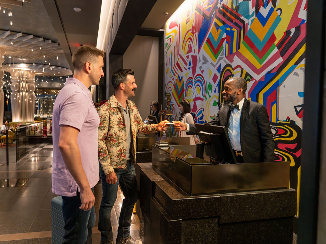 Un hôtel partenaire accueille deux clients à la réception du W Philadelphia, où une fresque murale géométrique aux couleurs vives et un design contemporain confèrent au hall d'entrée une ambiance dynamique.