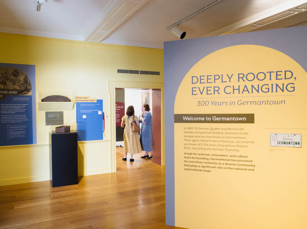 Visitors explore an exhibition in the Historic Germantown Visitor Center, with yellow and purple displays and artifacts displayed.