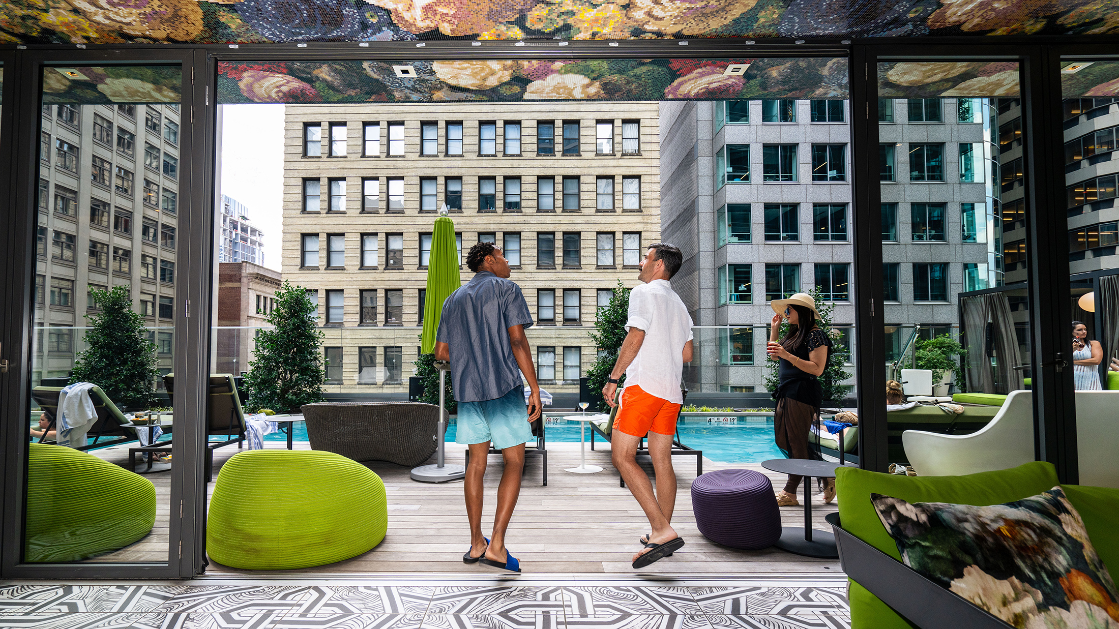 Les clients en maillot de bain se promènent et se détendent autour de la piscine sur le toit du W Philadelphia, au milieu des transats, d'une décoration colorée et avec vue sur les gratte-ciel de Center City.