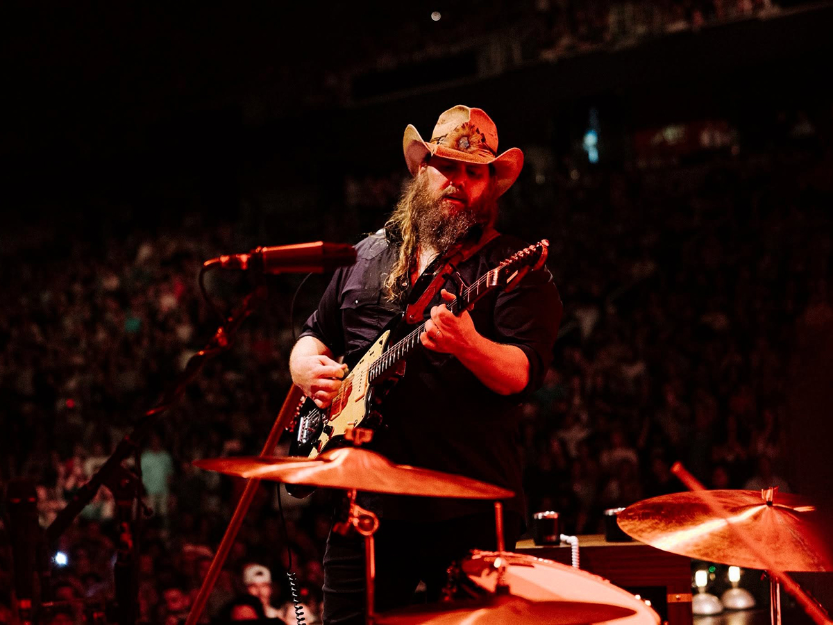 Country music artist Chris Stapleton performs onstage with an electric guitar under red stage lighting.