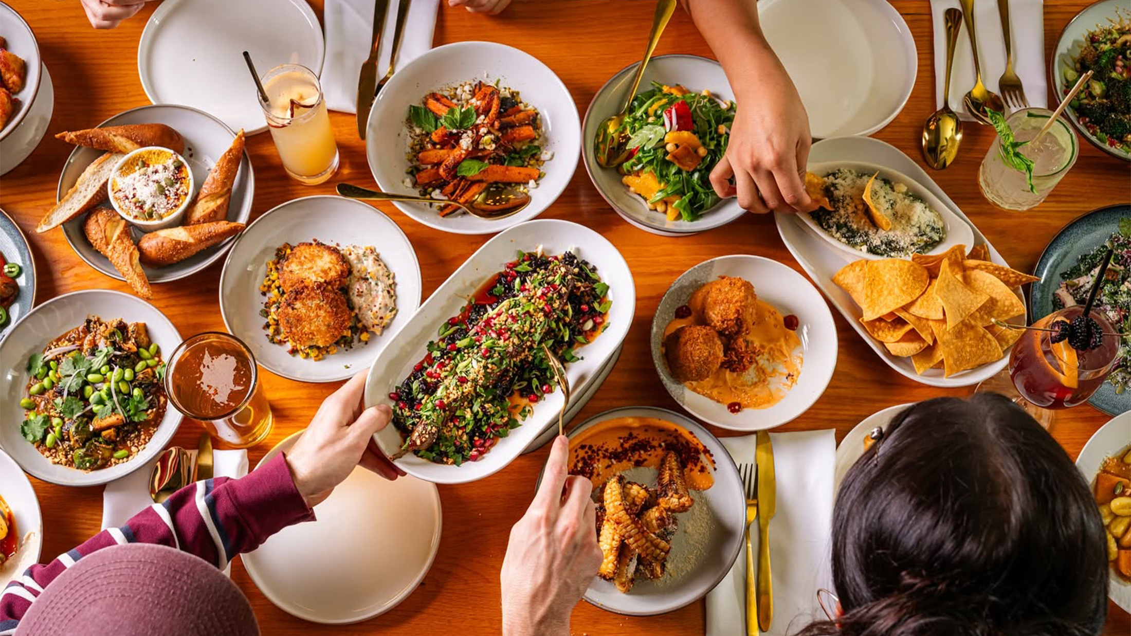 Una vista aérea de coloridos platillos para compartir, que incluyen ensaladas, aperitivos, verduras asadas y cócteles, dispuestos sobre una mesa en el restaurante Fitz on 4th de Filadelfia.