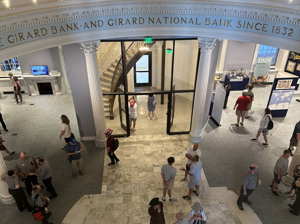 Vue d'en haut des visiteurs découvrant le grandiose hall de la First Bank, avec ses colonnes de marbre imposantes, ses détails architecturaux historiques et ses expositions muséales.