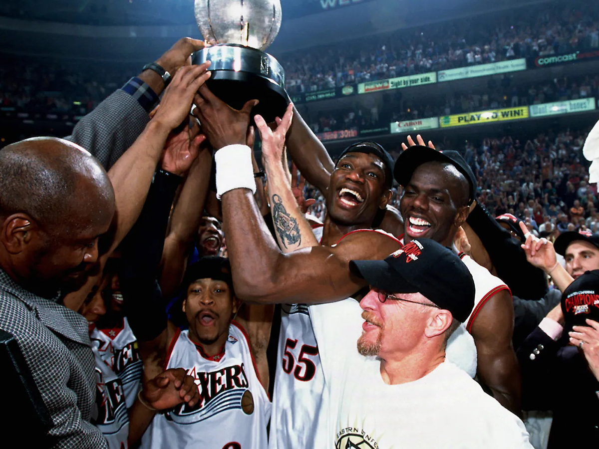 Les joueurs et le staff des 76ers de Philadelphie font la fête sur le terrain, brandissant au-dessus de leurs têtes le trophée d'argent du championnat au milieu d'une foule en liesse.