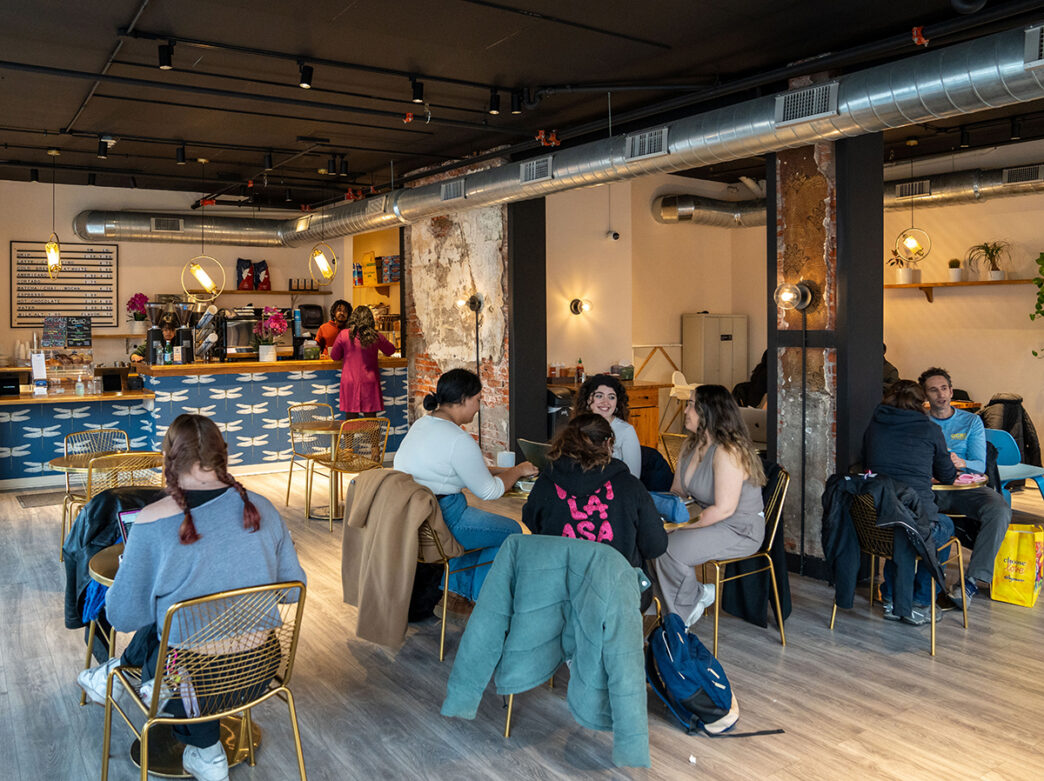 Customers work on laptops, chat and enjoy coffee inside Arterial Coffee, a spacious cafe with exposed brick columns, industrial ceilings and a colorful coffee bar.