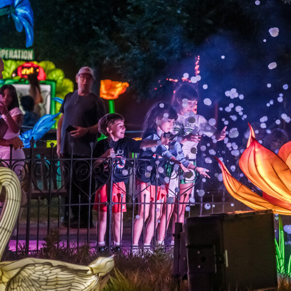 Drie kinderen spelen ’s avonds met zwevende zeepbellen naast een gloeiende lotusbloemlantaarn en een zwaanlantaarn tijdens het Chinese Lantaarnfestival in Philadelphia.