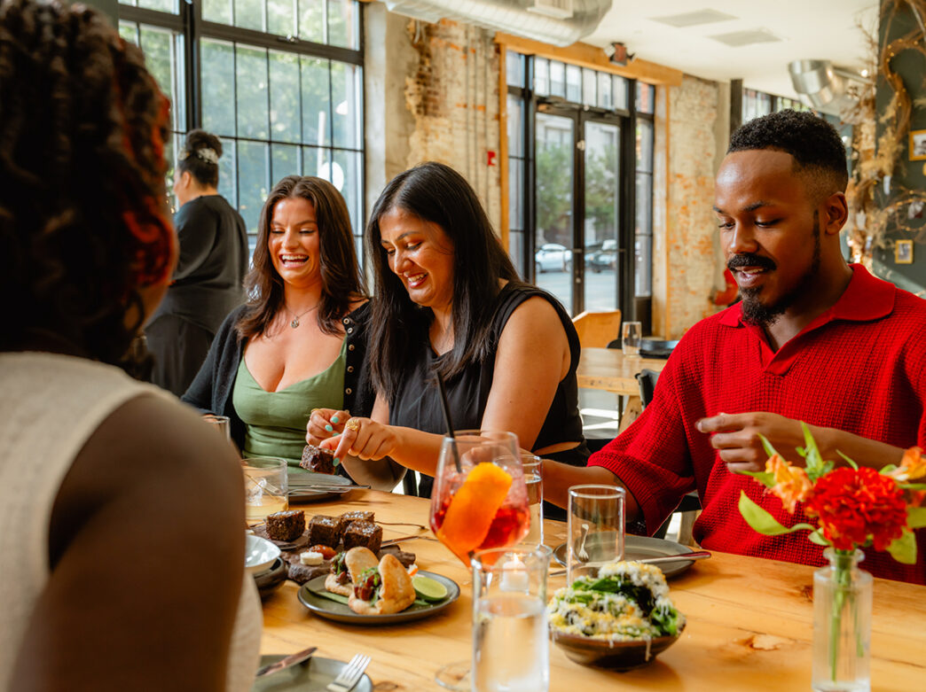 Diners gather around a wooden table, sharing small plates and conversation inside Honeysuckle's light-filled dining room.