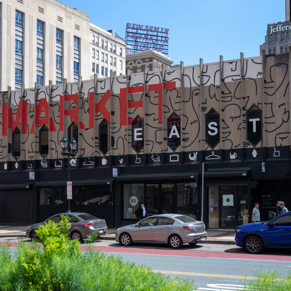 The exterior of a recently renovated building on Market Street, featuring a bold mural-like facade with overside MARKET EAST lettering, stylized line-art faces and storefronts at street level.