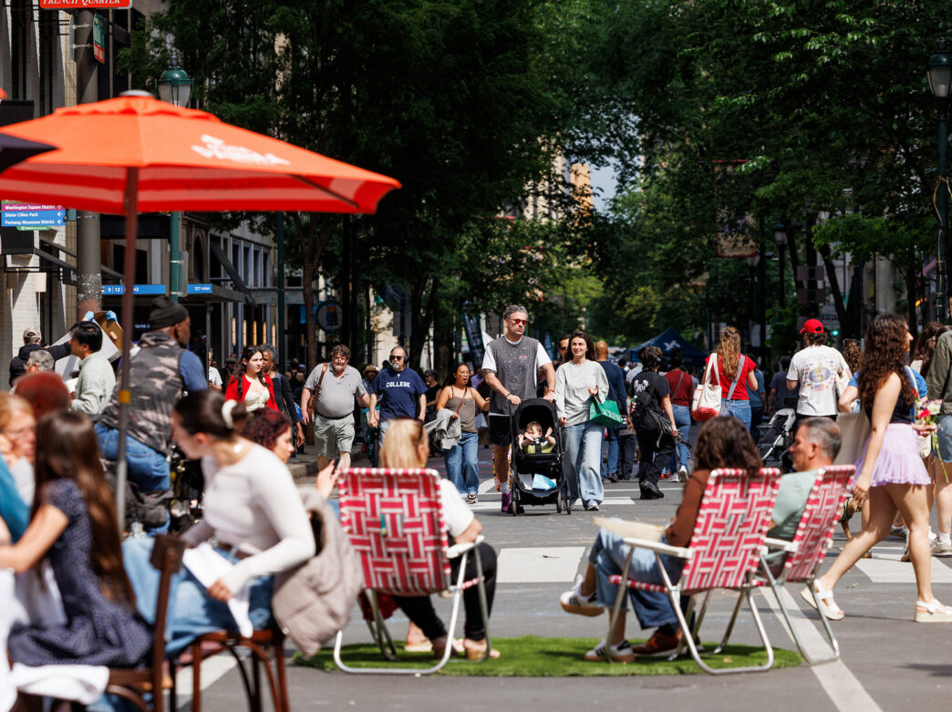 La foule se promène dans la rue Walnut, fermée à la circulation, à l'occasion de l'événement « Open Streets : West Walnut », tandis que les visiteurs dînent sous des parasols et se détendent dans des chaises longues installées sur la chaussée.