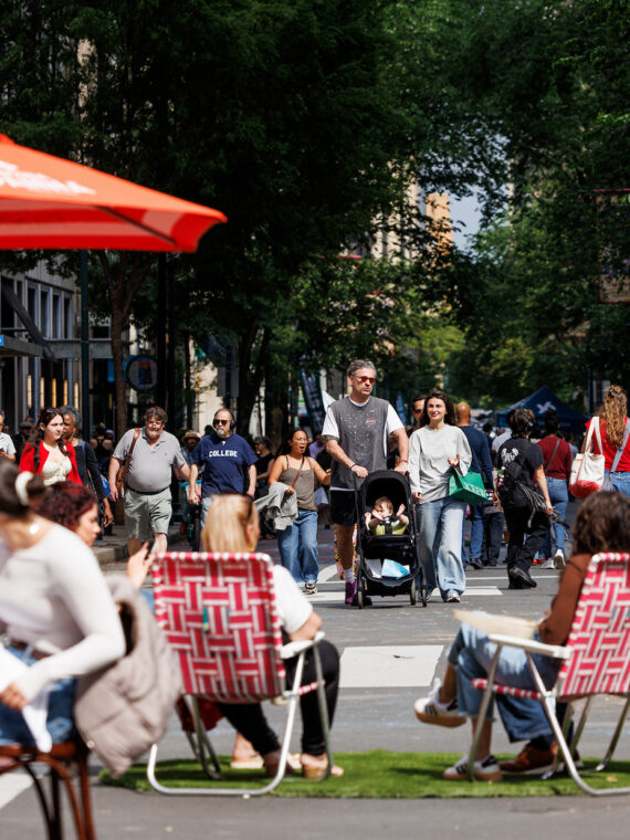 Crowds stroll along a car-free Walnut Street during Open Streets: West Walnut, while visitors dine beneath umbrellas and relax in lawn chairs set up in the roadway.