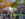 Crowds walk along paved pathways through colorful fall foliage at Peddler's Village during the Apple Festival, with vendor tents selling apple fritters and more.