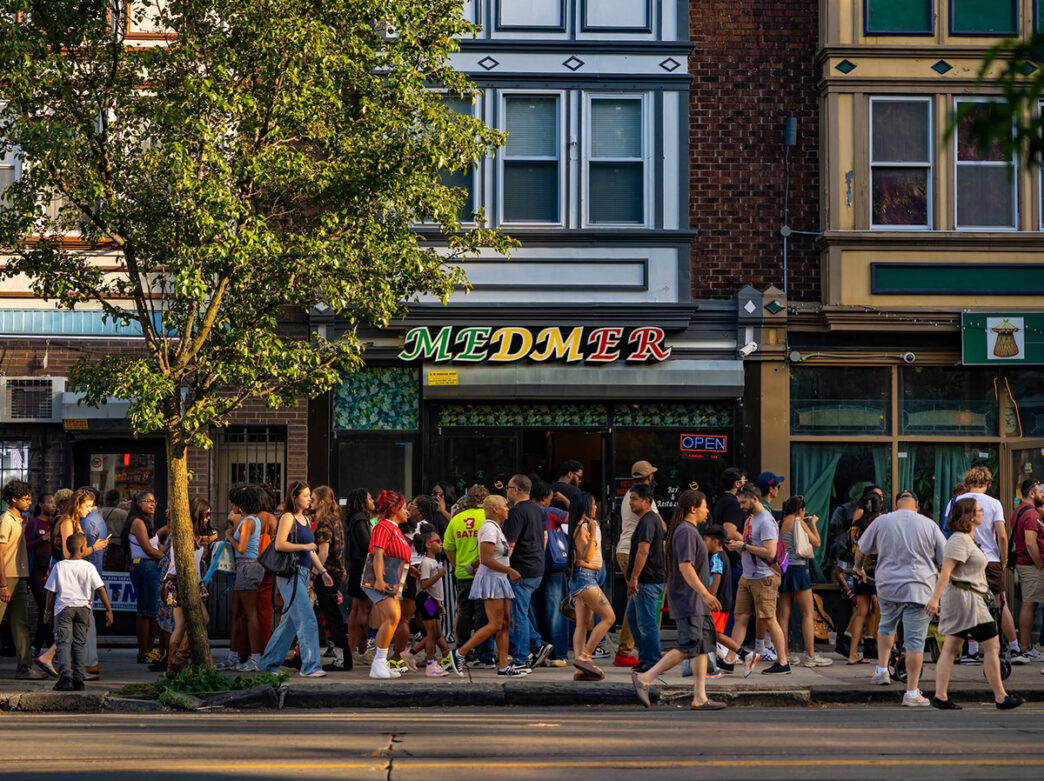 Crowds walk along a sidewalk past storefronts during the Baltimore Avenue Dollar Stroll.
