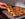 A hand lifts a thick Detroit-style pizza slice topped with melted cheese, tomatoes and herbs from a freshly baked pie.
