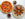 An overhead view of a pepperoni, mushroom and pepper pizza beside a plate of glazed chicken wings, with two glasses of iced soda on a white table.
