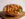 A large bowl of seasoned crab legs, shrimp, corn, potatoes and greens sits on a wooden serving board.