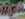 A large pack of competitive cyclists round a bend during a road race as a photographer captures the action from the roadside.