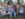 Three children pose with a straw scarecrow sitting on the ground at the Perkasie Fall Festival, with hay, trees and additional scarecrows int he background.