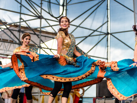 Three dancers in flowing turquoise and orange costumes twirl and perform a traditional Indian dance on an outdoor stage during Philadelphia's Festival of India.