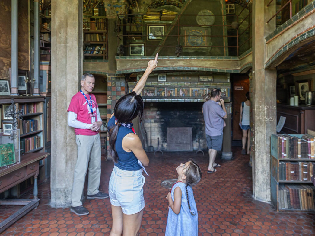 A woman and young child look up at the ornate interior of Fonthill Castle during a visit, surrounded by bookshelves, tilework and historic furnishings. A tour guide stands in the background.