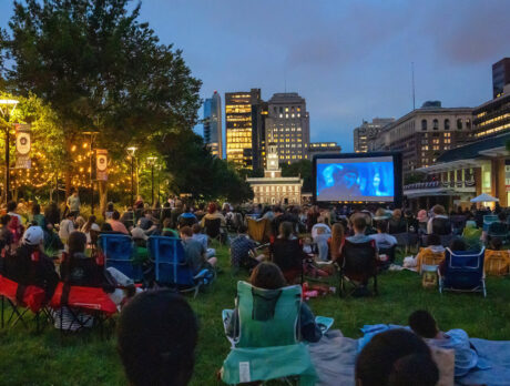 Une foule nombreuse se rassemble sur la pelouse de l'Independence Mall pour une projection en plein air du film « National Treasure » à la tombée de la nuit, avec le Independence Hall visible derrière le grand écran de cinéma.
