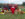 A costumed apple mascot sittings on a bale of hay in front of a vintage red tractor decorated with pumpkins, mums and other fall decor.