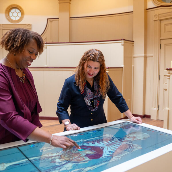 Two people explore a digital anatomical model of the human body on an interactive Anatomage table inside the Pennsylvania Hospital Museum.