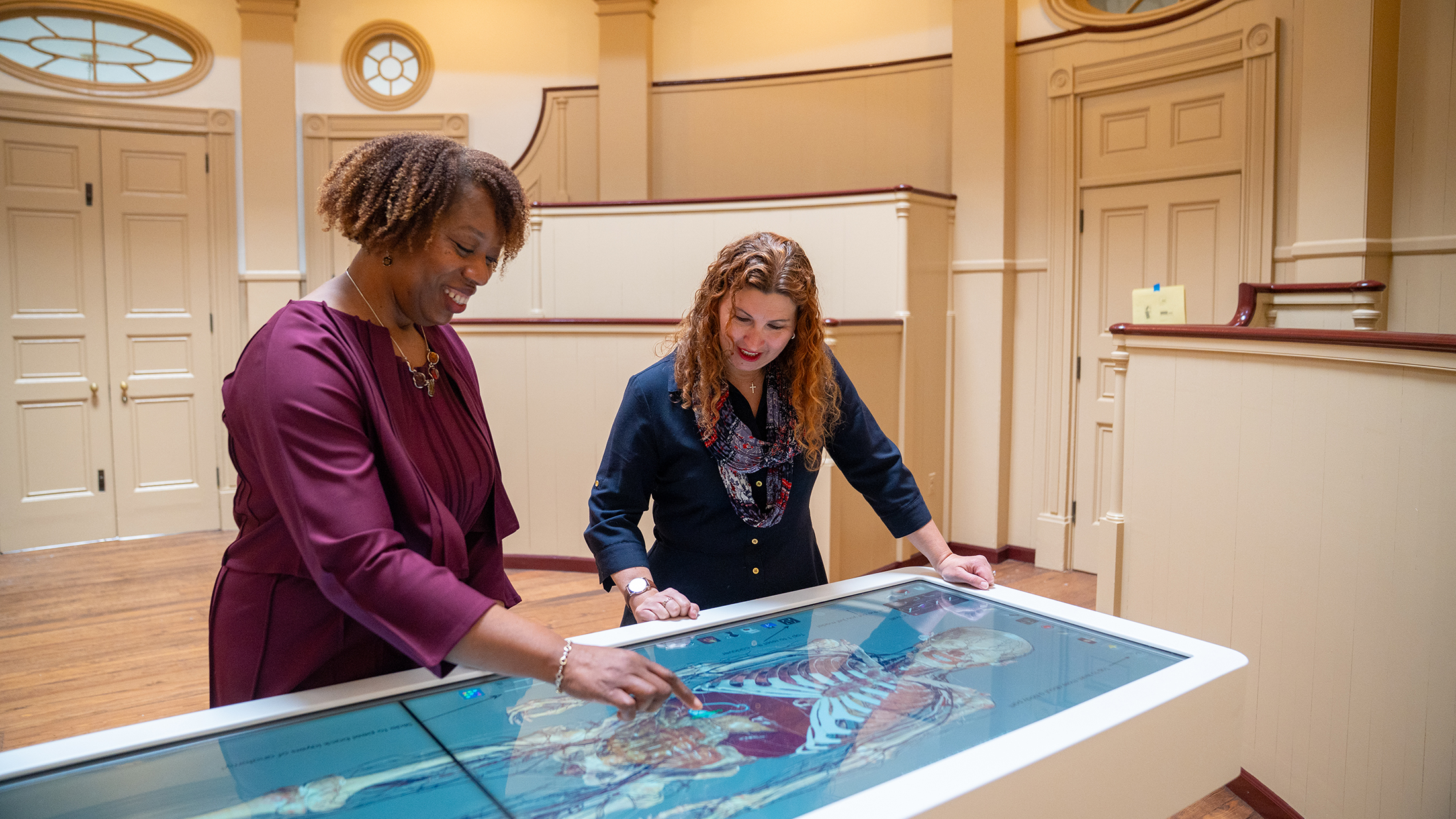 Two people explore a digital anatomical model of the human body on an interactive Anatomage table inside the Pennsylvania Hospital Museum.