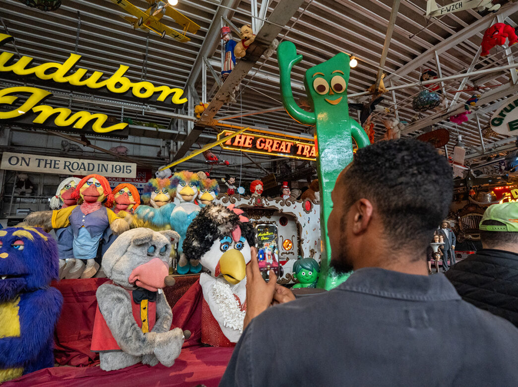 A visitor photographs a colorful collection of vintage characters and figures, including a towering green Gumby.