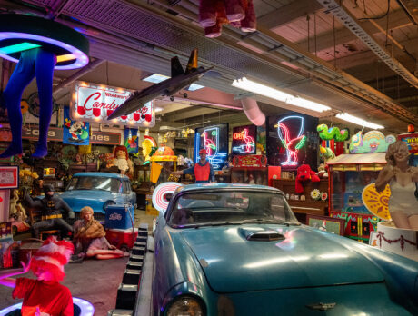 A vintage blue convertible is surrounded by colorful neon signs, toys, figures and other nostalgic memorabilia inside the American Treasure Tour Museum.